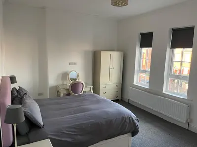 a bedroom with a bed and a dresser and two windows at Chestnut House in Southport