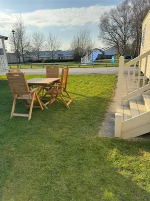 two wooden chairs and a table in the grass at Miarlo Lodge Derwent Haven Lakeland in Grange Over Sands