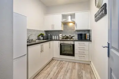 a kitchen with white cabinets and a wooden floor at Liverpool 3 Bedroom Contractor Stay Cherry House in Liverpool