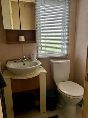 a bathroom with a sink and a toilet and a window at Metcalfes family caravan in Heysham