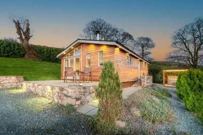a log cabin with a stone wall and a patio at Haven Lodge Kirkby In Furness, with views to the estuary and hot tub, ideal romantic break in Soutergate