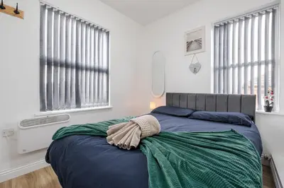 a bedroom with a bed with a blanket and two windows at TopFloor Apt LikeHome Long-Term Free Parking in Liverpool