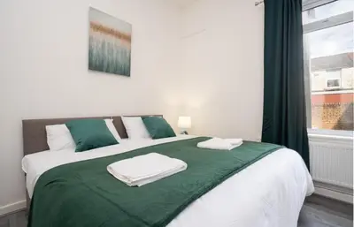 a bed with green and white sheets and a window at Property is sold in Liverpool