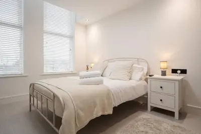 a white bedroom with a bed and a night stand at Cosy Nook Kitchen w Washer & SofaBed Parking in Liverpool