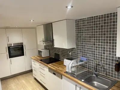 a kitchen with white cabinets and black tiles on the wall at Beach House Courtyard 2 bed in Southport