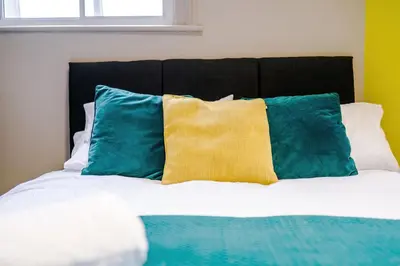a bed with blue and yellow pillows on it at Stylish 2 Bedroom Apartment in Central Wigan by MDGC Developments Ideal For Weekends Away and Business Guests in Wigan
