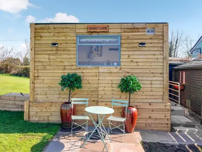 a small wooden building with a table and two plants at Sunset Cabin in Ormskirk