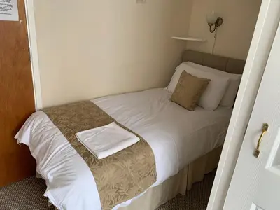 a small bedroom with a bed with white sheets and pillows at Sharn Bek Hotel in Blackpool