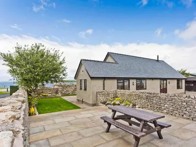 a house with a stone wall and a wooden bench at Keer Cottage in Carnforth