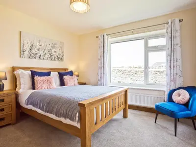 a bedroom with a bed and a window and a blue chair at Keer Cottage in Carnforth