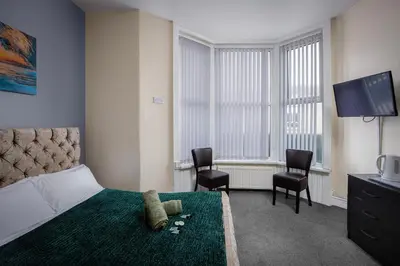 a bedroom with a bed and two chairs and a television at The Ocean Inn in Blackpool