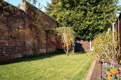 a brick wall with a red hose next to a yard at Bradley's Hideaway With Private Garden in Eccleston
