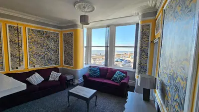 a living room with purple couches and a large window at 6 Cocker Square in Blackpool