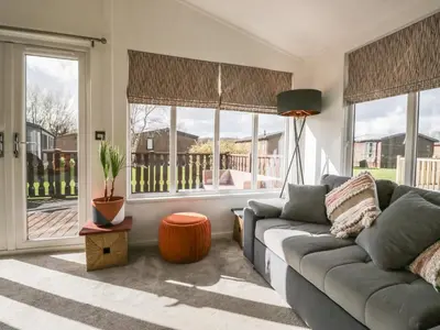 a living room with a gray couch and windows at Gressingham View Lodge in Carnforth