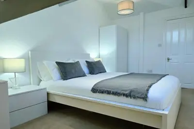 a white bedroom with a large white bed with a nightstand at Stylish City Centre Apartment With Parking in Preston