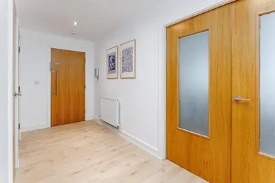 an empty hallway with a wooden door and white walls at Flatzy - Prime City Apartment with Free Parking & Ping Pong Table in Liverpool
