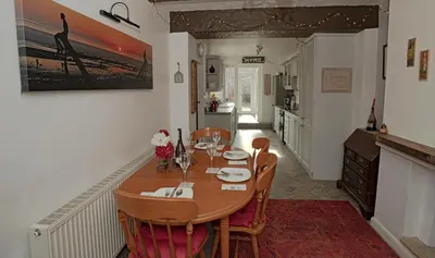 a dining room with a table and a kitchen at Smithy Cottage in Heysham