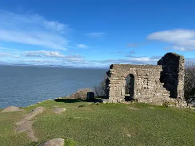 an old stone building on a hill next to the ocean at Smithy Cottage in Heysham