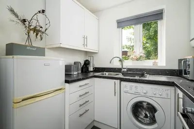 a kitchen with white cabinets and a washer and dryer at The Acorn Nook - Central Stay in Liverpool