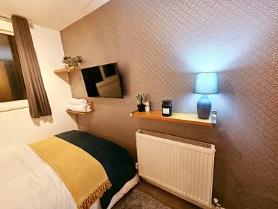 a room with a bed with a lamp and a tv at Platt House in Wigan