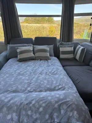 a bed with pillows and a couch in front of a window at 148 Port Haverigg in Millom