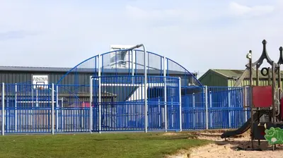 a playground with a blue gate in a park at Riverside Holiday Park in Banks