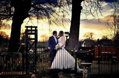 a bride and groom standing next to a fence at Briars Hall Hotel in Burscough