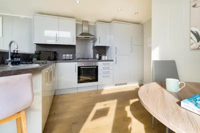 a kitchen with white cabinets and a wooden floor at Silverdale Lodge, HotTub, Wi-FI, Quiet & Sleeps 4 in Warton