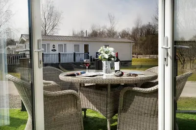 a table with a glass of wine and flowers on a patio at Silverdale Lodge, HotTub, Wi-FI, Quiet & Sleeps 4 in Warton