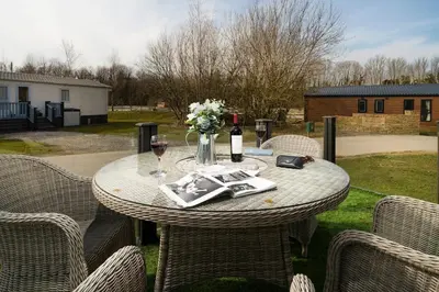 a table with a bottle of wine and flowers on it at Silverdale Lodge, HotTub, Wi-FI, Quiet & Sleeps 4 in Warton