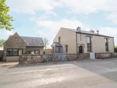 a white house with a stone wall next to a street at Stoneycross Cottage in Preston