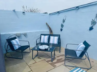 a patio with two chairs and a table and a wall at Willow Cottage Haverigg Millom in Haverigg