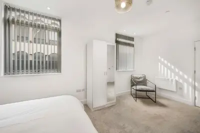 a white bedroom with a bed and a chair at GuestReady - Gladstone in Liverpool