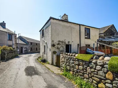 an old house with a stone wall next to a street at Rainbow Cottage in Vickerstown