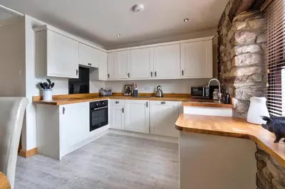 a kitchen with white cabinets and a stone wall at The Old Paper-shop, WiFi, Sleeps 4 & Pet Friendly in Bolton le Sands
