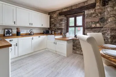 a kitchen with white cabinets and a stone wall at The Old Paper-shop, WiFi, Sleeps 4 & Pet Friendly in Bolton le Sands