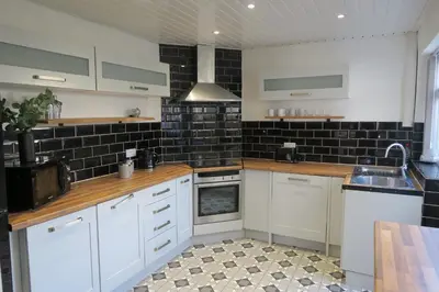 a kitchen with white cabinets and black tiled walls at NEW 4 Bed house close to train station and town in Blackpool