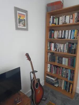 a guitar is sitting next to a book shelf at Double room, living space and bathroom, in a family home, near Ulverston in Pennington