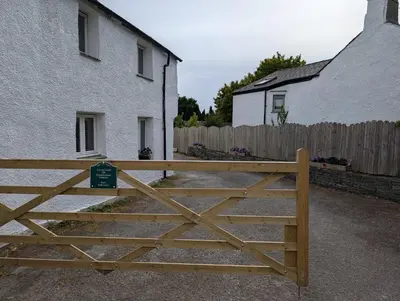 a wooden gate in front of a house and a fence at Garth Nook Barn in Soutergate