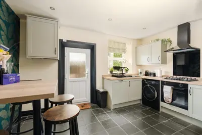 a kitchen with white cabinets and a table and stools at Elsie's Cottage in Ribchester