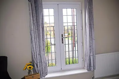a window with curtains and a vase of flowers on a window sill at Thirlmere in Upholland