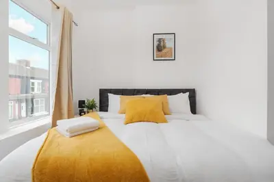 a white bed with yellow pillows and a window at Entire 4 Bedroom house in Bootle Liverpool-Ideal for contractors, family and group-Free Parking & Free internet-Sleeps 7 in Litherland