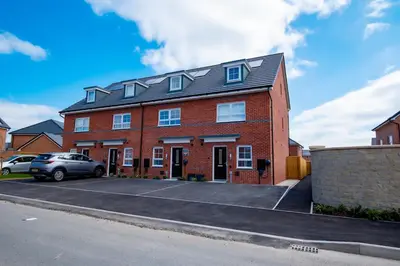 a red brick building with a car parked in a parking lot at Luxury 5BDR with City Access, Free Parking and Wi-Fi in Ince-in-Makerfield