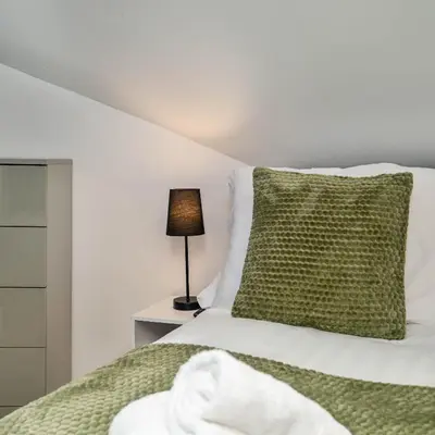 a bedroom with a bed with a green pillow and a lamp at Beautiful 3BR Flat near LFC Stadium - Sleeps 8 in Liverpool