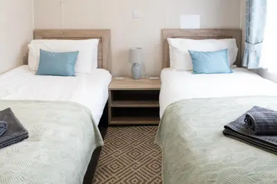 two beds in a hotel room with blue pillows at Bittern Lodge: 3BD Retreat in South Lakeland Park in Borwick