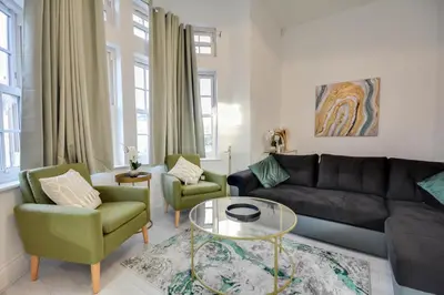 a living room with a black couch and two green chairs at Cosy Wigan Apartment with Sunny Views in Wigan
