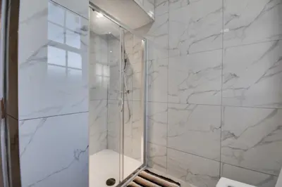 a bathroom with a shower with white marble walls at Cosy Wigan Apartment with Sunny Views in Wigan