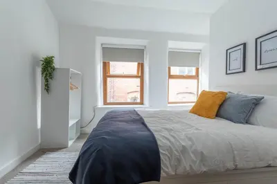 a white bedroom with a bed and two windows at Fisherman's Cottage by the sea in Morecambe