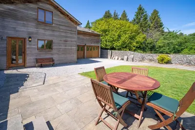 a patio with a wooden table and chairs in a yard at Leighton Banks in Beetham
