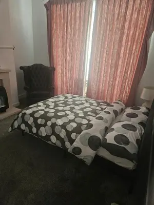 a bed with a black and white comforter and a window at Olive Guest House in Bolton